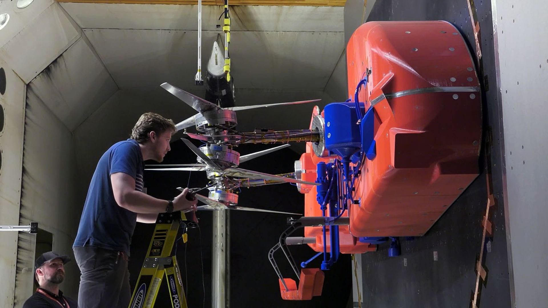 Technicians installing rotors onto a full-scale half-model of the Dragonfly spacecraft inside a wind tunnel for testing. ©NASA